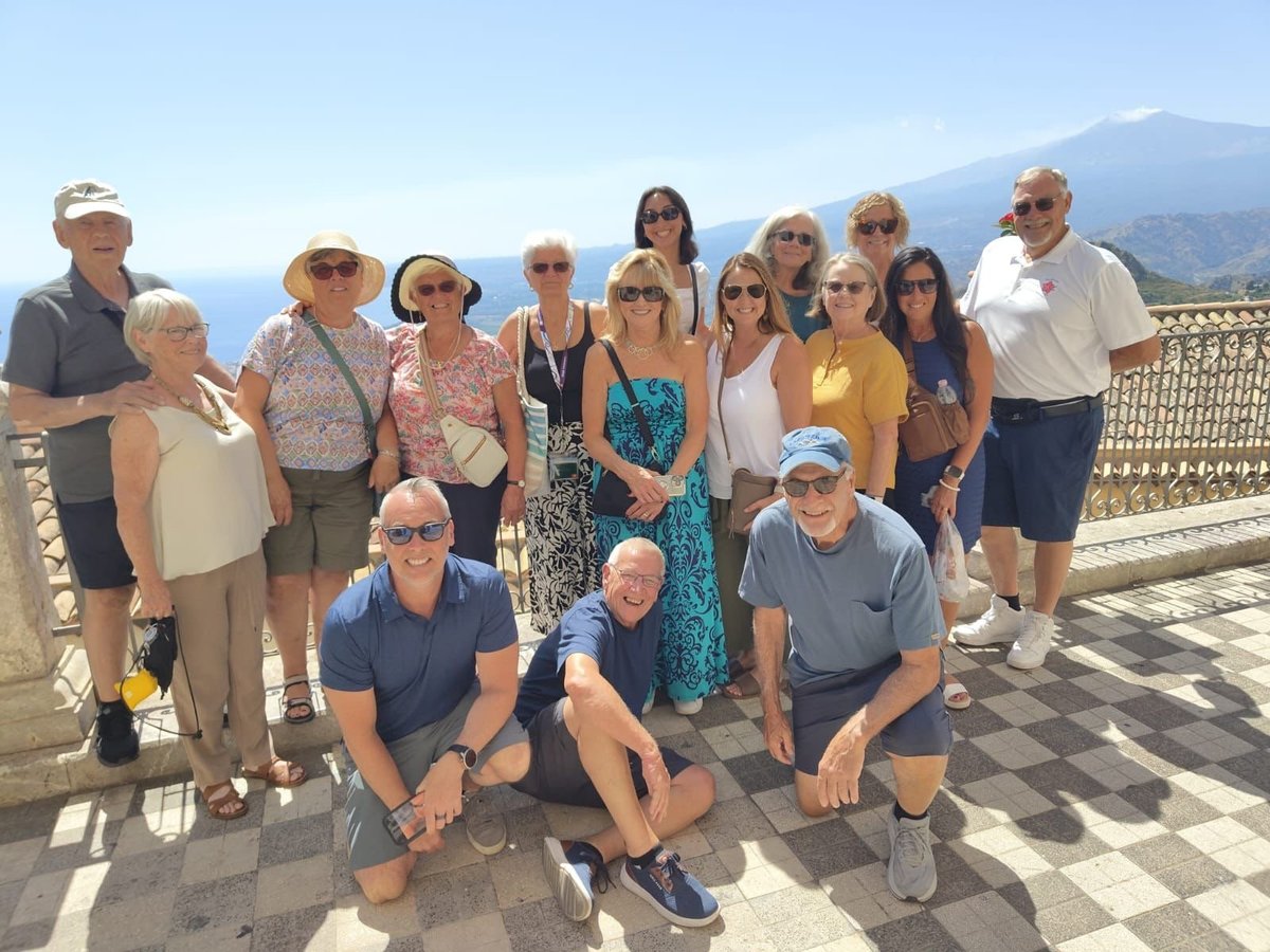 Group of tourists posing on a scenic rooftop terrace with a coastal mountain backdrop