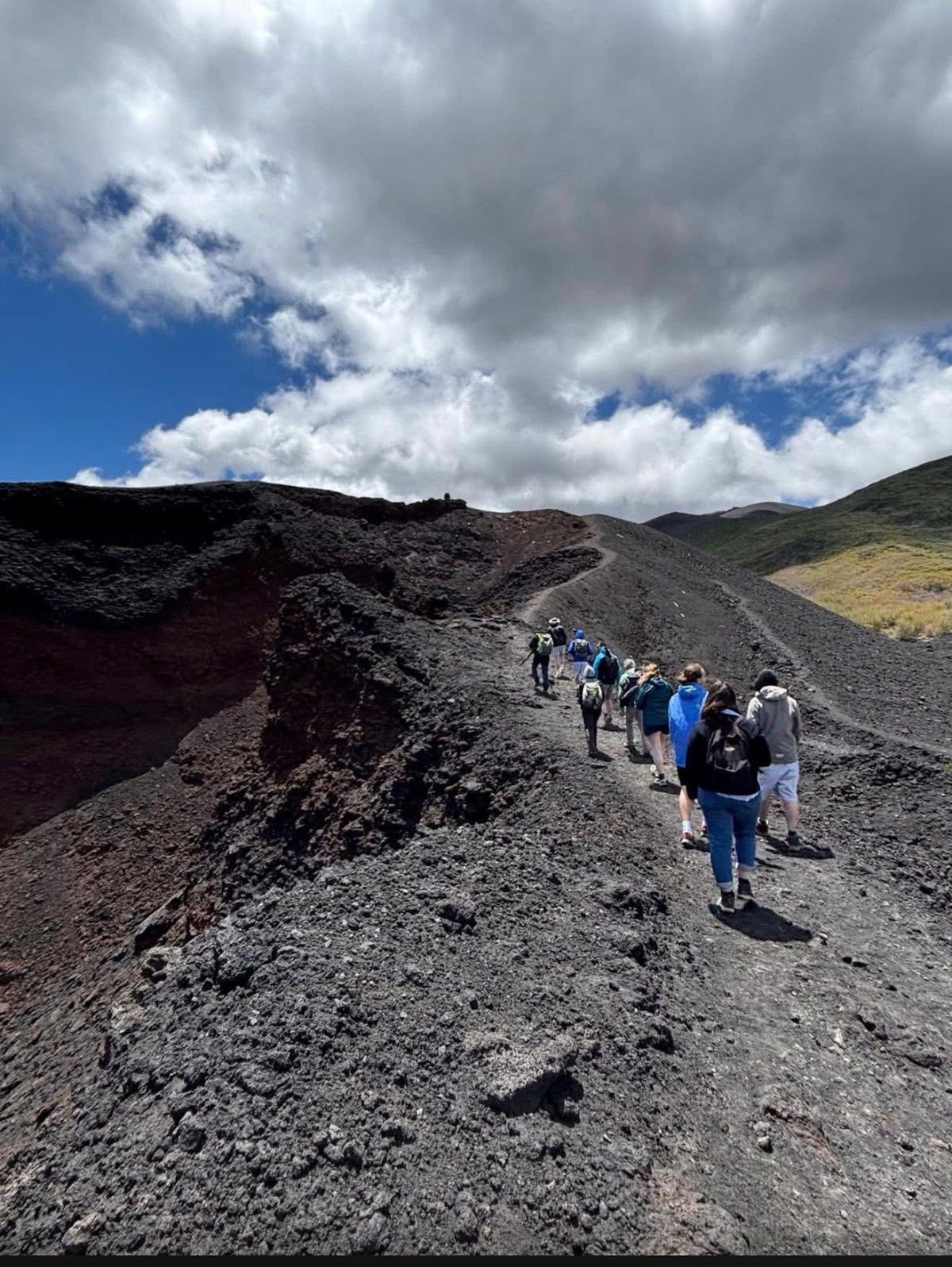 Group of hikers walking on a volcanic lava field with dramatic cloudy sky and mountains in the background