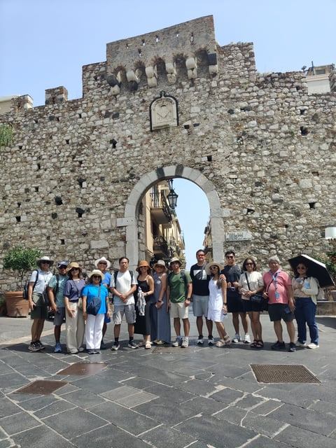 Large group of tourists posing at historic stone gate with arched entrance in old town center