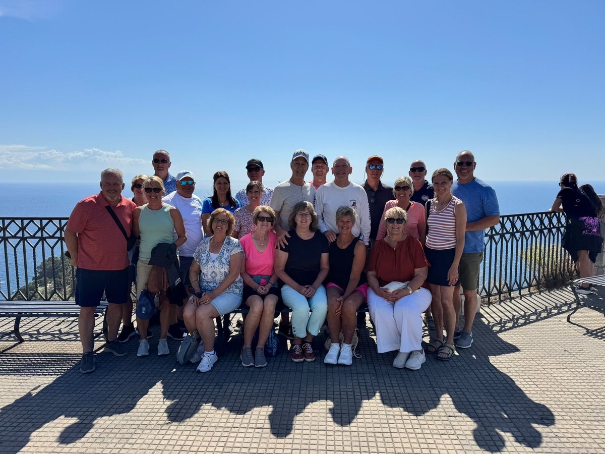 Large group of people posing together on a scenic overlook with ocean and blue sky in background
