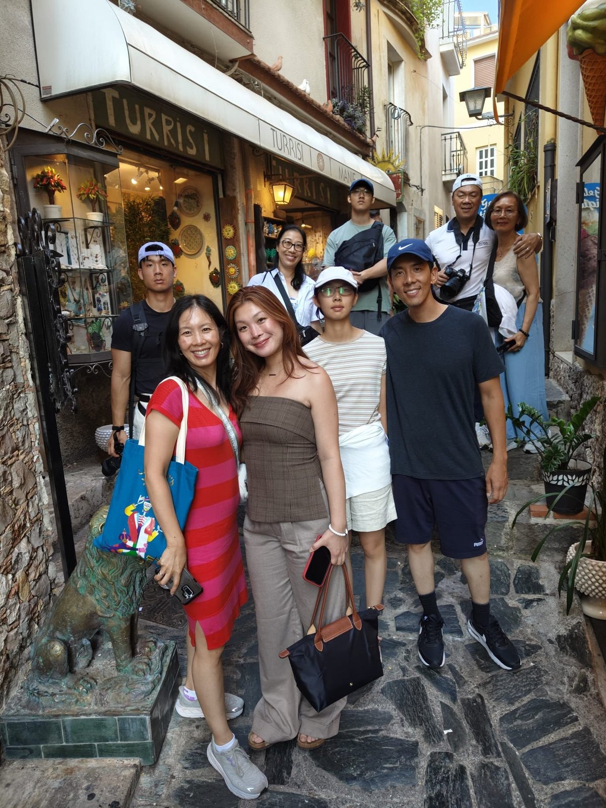 Group of tourists posing together on a narrow cobblestone street in front of a Turkish shop with stone buildings