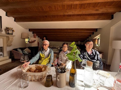 Four people seated at a dining table in a modern home with wooden beams, smiling during a meal together