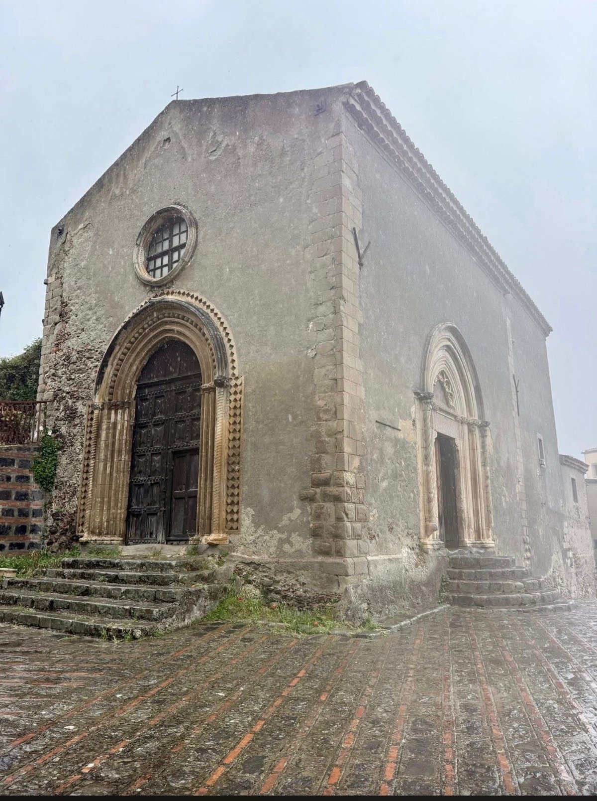 Weathered stone chapel with arched doorway, circular window, and red brick courtyard
