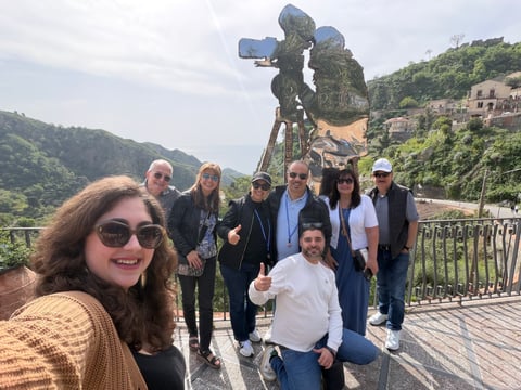 Group of tourists posing on a mountain overlook with a large telescope and scenic valley landscape in the background