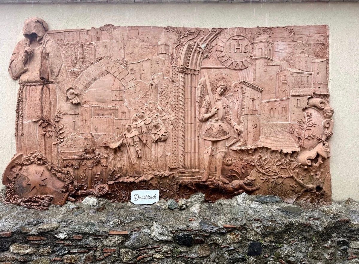 Ancient terracotta relief panel with carved figures, architectural elements, and hieroglyphic-style inscriptions displayed on a stone base