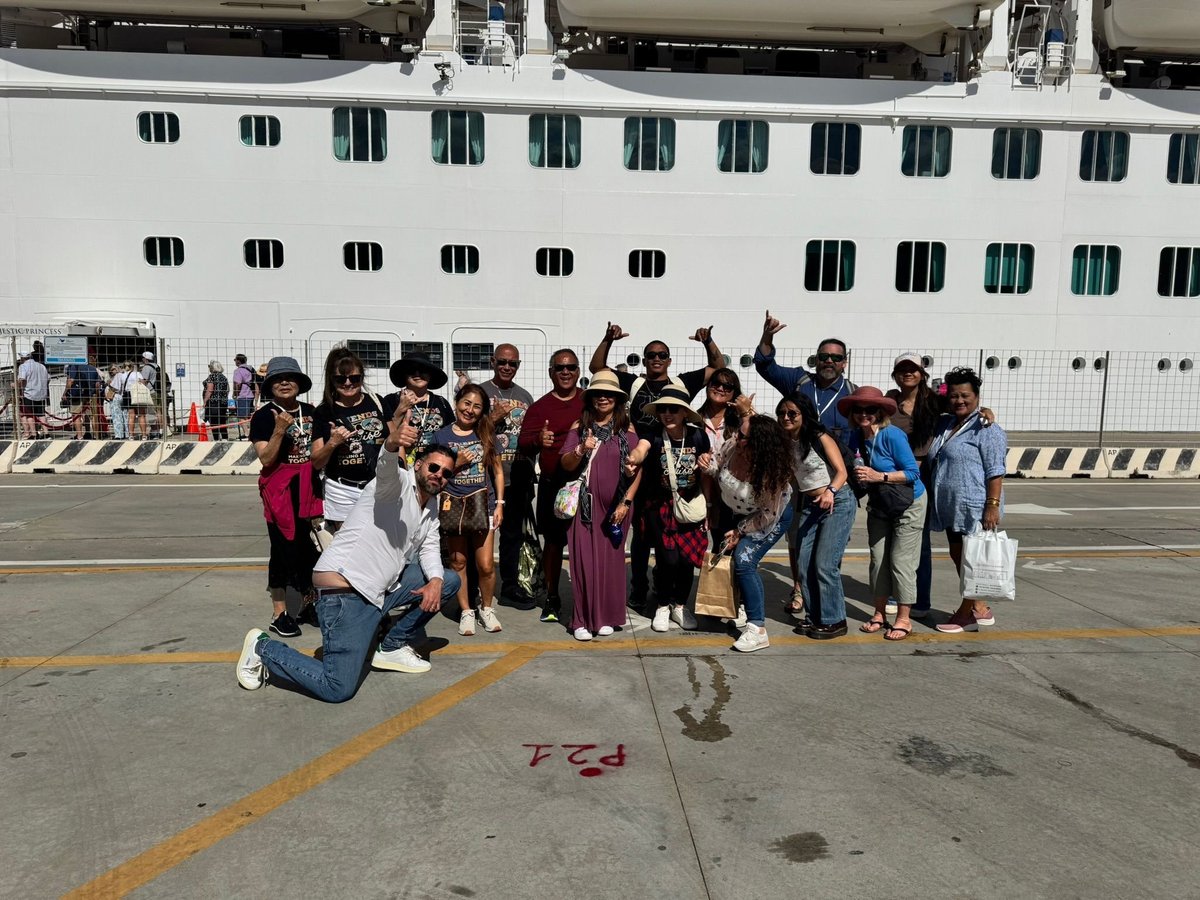 Large group of people posing together in front of a white cruise ship docked at port