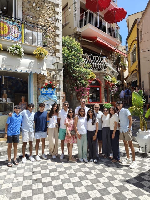 Group of people posing together in a colorful Mediterranean-style town square with historic buildings and red umbrellas