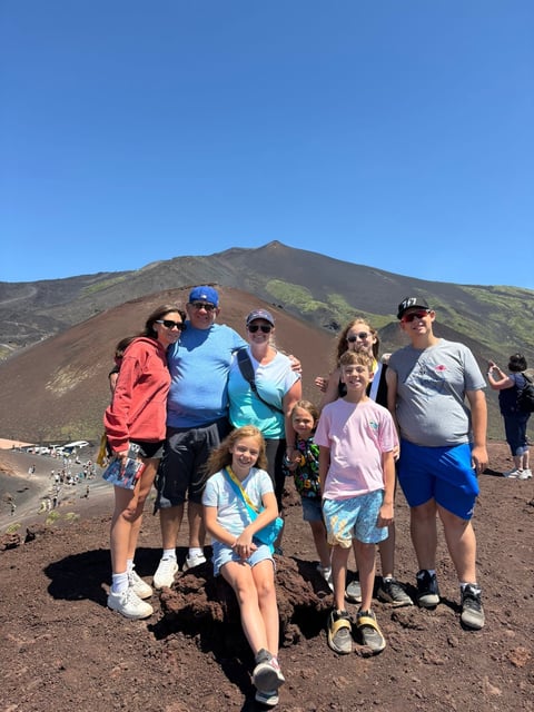 Group of people posing on volcanic ash slope with cinder cone mountain in background under clear blue sky