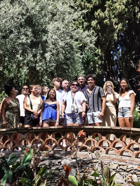 Group of tourists standing on a wooden bridge in a lush garden with tall trees and tropical plants