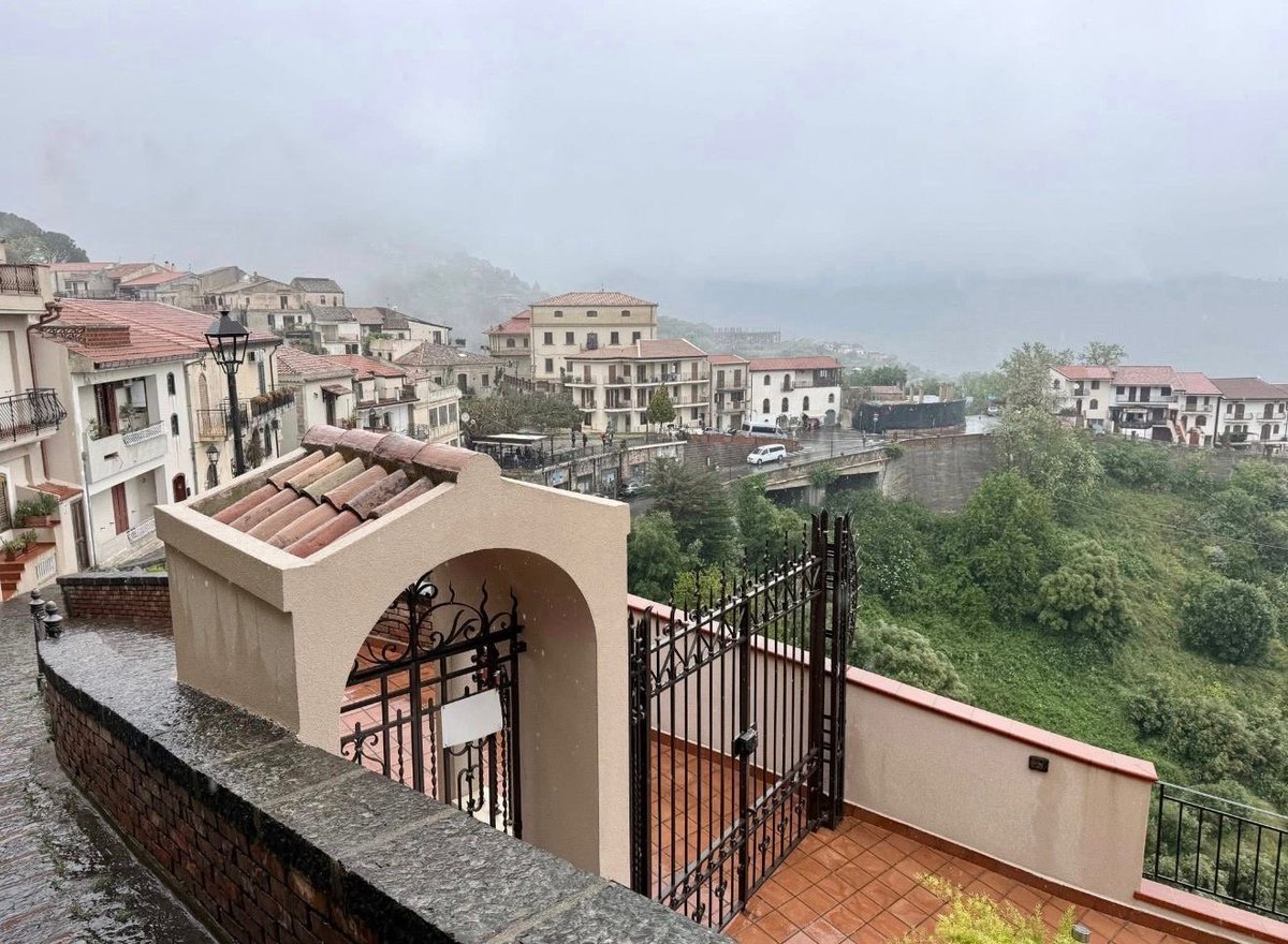 Rooftop terrace with arched structure and wrought iron gates overlooking a misty hillside town with buildings