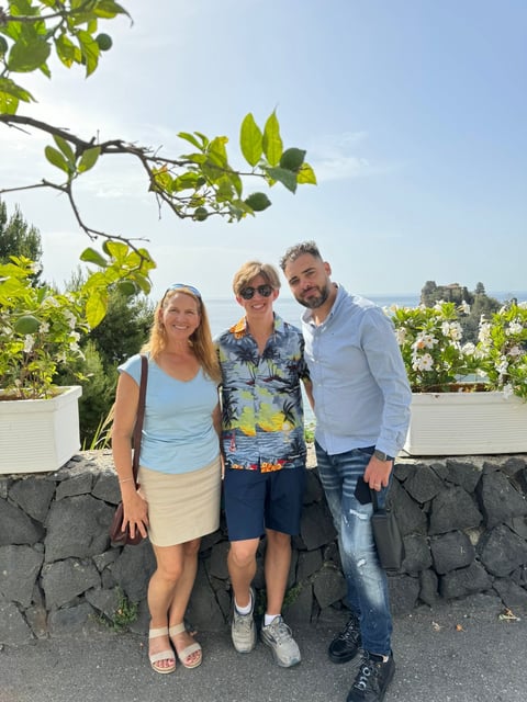 Three people smiling at camera in front of stone wall with tree branches and scenic hillside view