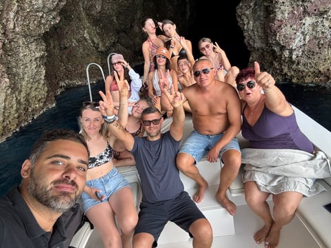 Group of people on a boat giving thumbs up gestures inside a cave, wearing casual summer attire