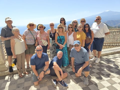 Group of tourists posing together on a terrace with mountain and coastal views in the background
