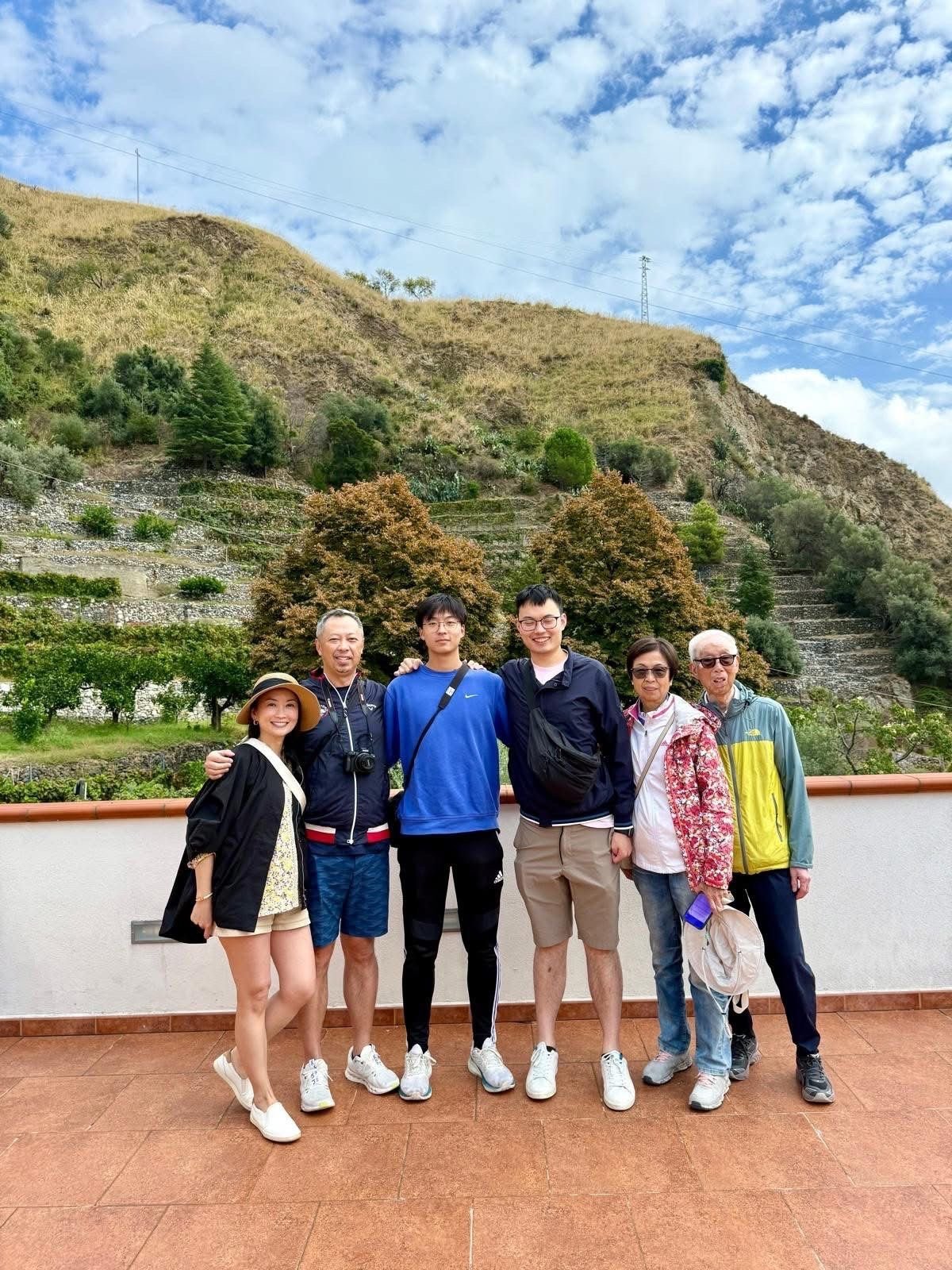 Group of six people standing together on a terracotta patio with a terraced hillside and blue sky in the background