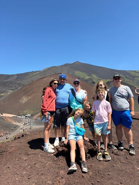 Group of family and friends posing together on dark volcanic slopes with a large cinder cone mountain in the background under clear blue sky