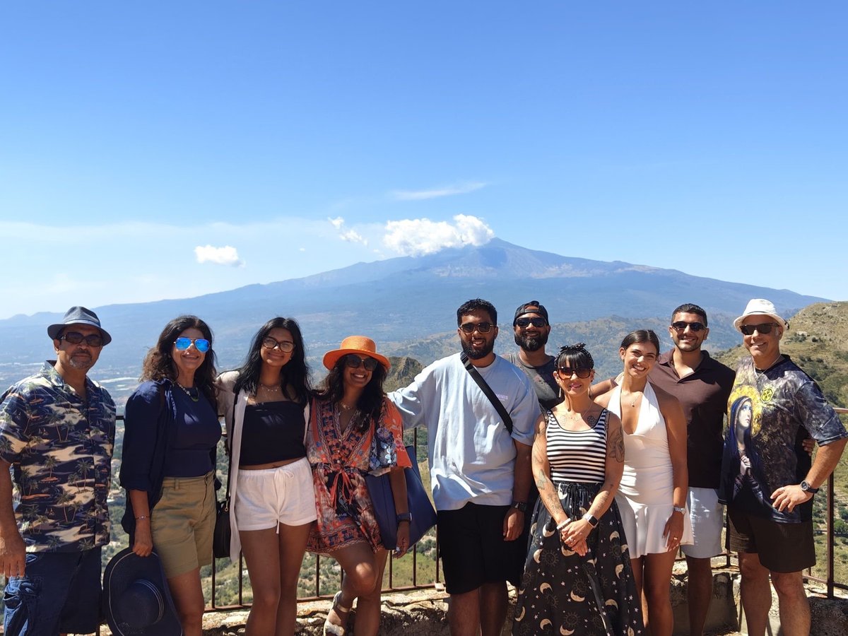 Group of ten people posing together outdoors with a snow-capped volcano mountain in the background under clear blue sky