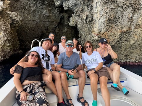 Group of people sitting on a boat in front of large rocky cliffs, enjoying a scenic water tour or excursion