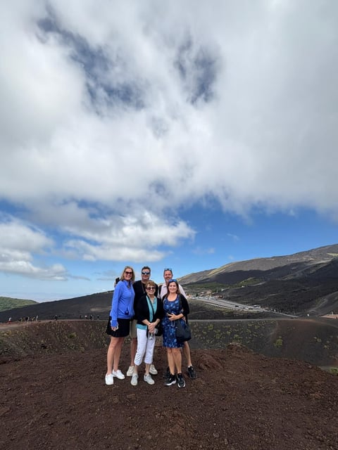 Four people standing together on a volcanic landscape with dark lava fields and mountains under a partly cloudy sky