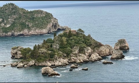 Rocky island covered in lush green vegetation surrounded by turquoise ocean water and smaller rocky outcrops