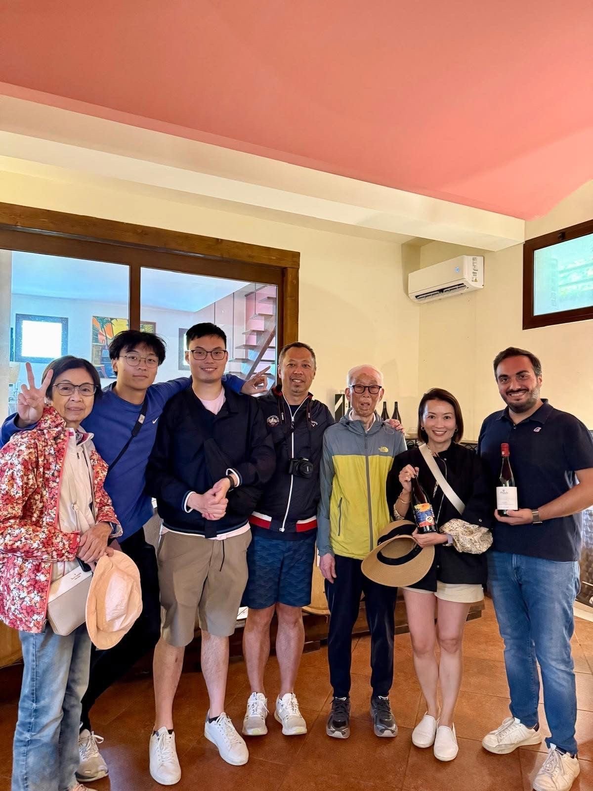 Group of eight people smiling at camera in indoor room with pink ceiling and wood flooring