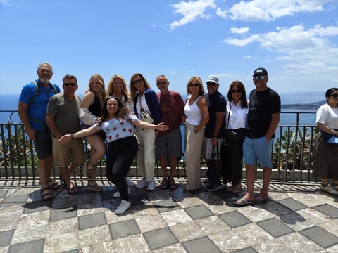 Group of people posing together on a waterfront overlook with a railing and ocean view in the background