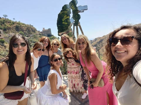 Group of women smiling at a scenic hilltop location with a large telescope or viewing scope and mountains in the background